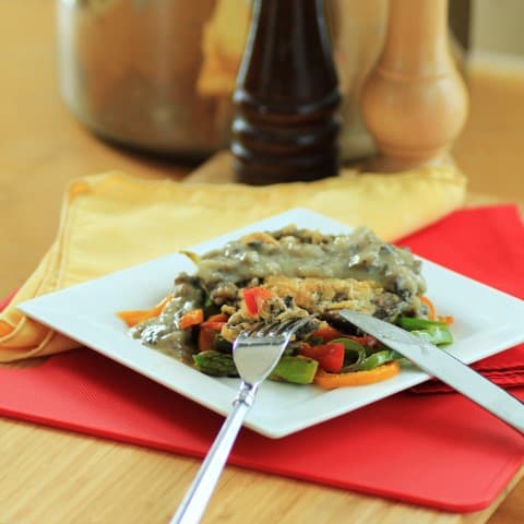 Chicken Fried Portobello Mushrooms on top of cook peppers with shallot gravy and a knife and fork