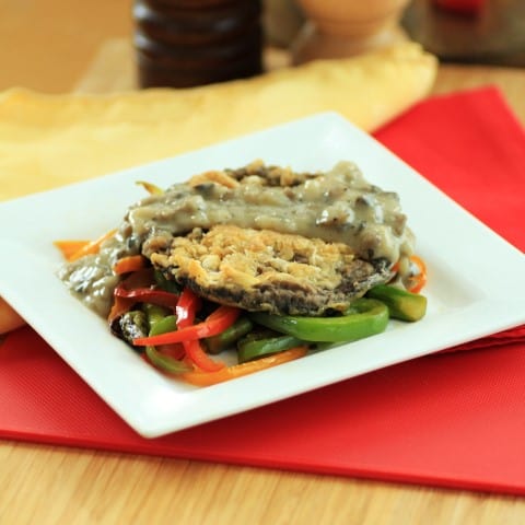 Chicken Fried Portobello Mushrooms on a white plate on top of cooked peppers with shallot gravy on top 