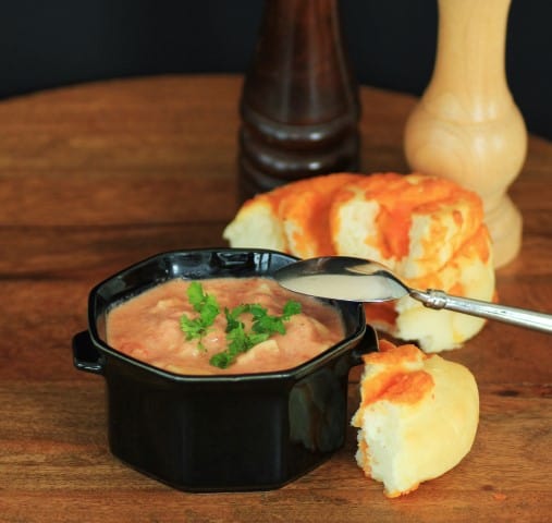 Cream of Tomato Soup with Tortellini in a black bowl with a spoon and cheese bun on a wooden board