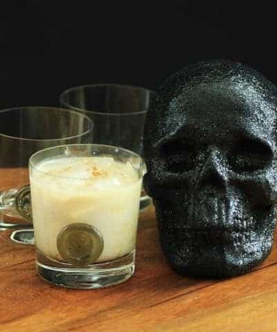 Heads Will Roll Cocktail in an old fashion glass sitting beside a black skull