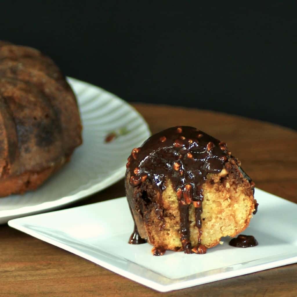 Snickers Bundt slice on a white plate with chocolate caramel peanut sauce pour over top