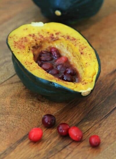 Roasted Acorn squash half with cranberries in the middle on a wooden board