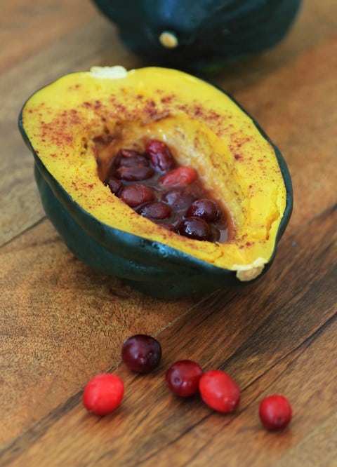 Acorn Squash with Cinnamon and Cranberries on a wooden board with fresh cranberries on the board