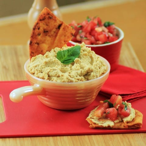 Classic Mediterranean Hummus in a white bowl with pita chips and diced tomatoes on a red napkin