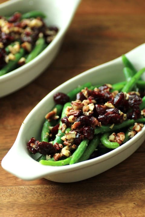 Green Beans with Pecans and Cranberries in a white oval serving dish on a wooden board