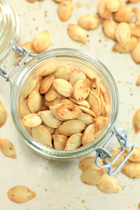 Roasted Pumpkin Seeds in a small glass mason jar with some scattered around the jar