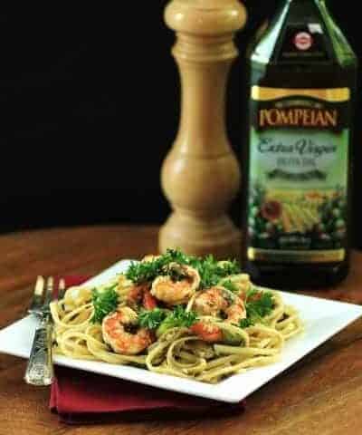 Shrimp and Linguini Olio pasta on a square white plate with a fork and a bottle of olive oil in the background