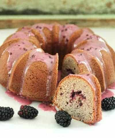 Triple Blackberry Bundt cake with a slice cut and fresh blackberries beside it.