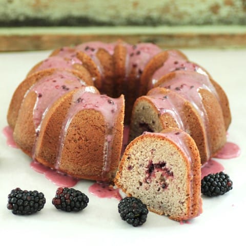 Triple Blackberry Bundt  with a slice cut out and and blackberries around the cake