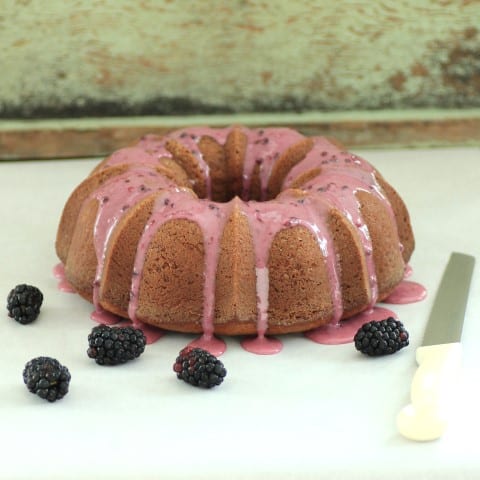 Triple Blackberry Bundt on a white board with blackberries around the cake and a large knife laying beside it.