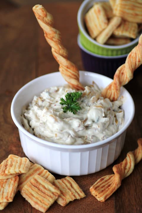 Caramelized Onion and Bacon Dip in a white bowl with bread sticks and crackers around the bowl
