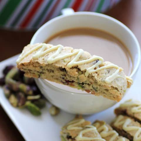 Cranberry Pistachio Biscotti sitting on top of the rim of a cup of coffee