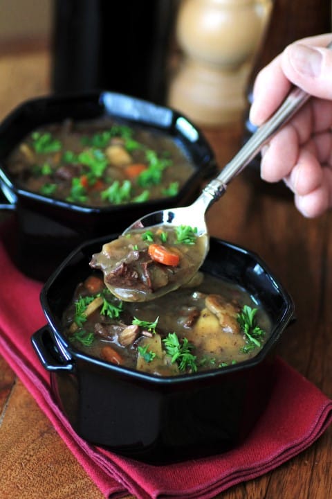 Beef, Wine and Mushroom Soup in a black soup bowl with a spoon scooping some soup