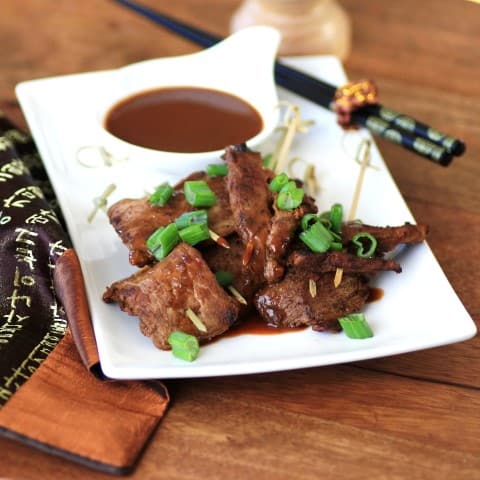 Easy Pork Peanut Satay on a white plate with dipping sauces and garnished with chopped green onions