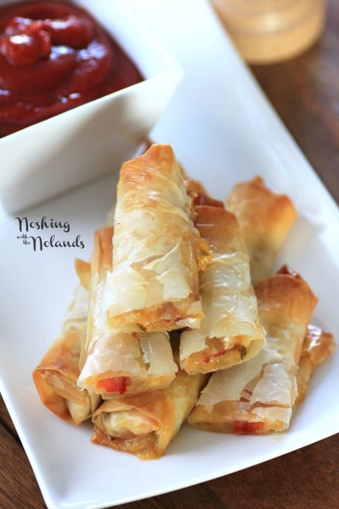 Italian Spring Rolls stacked on a white plate with dipping sauce in a white bowl