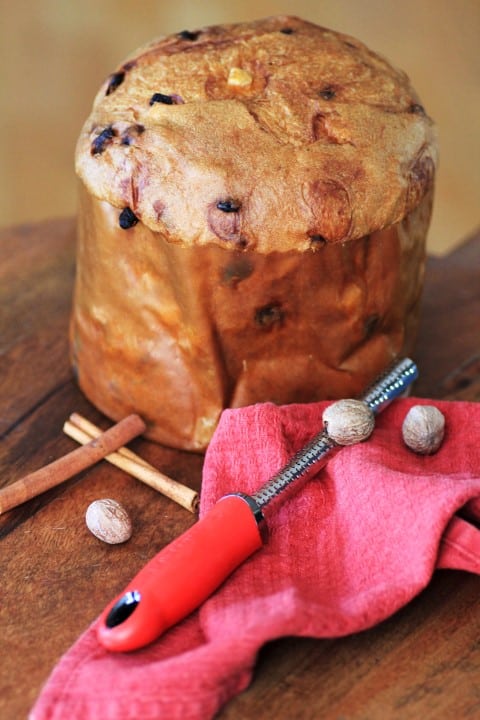 Panettone loaf on a wooden cutting board with whole nutmeg and cinnamon sticks