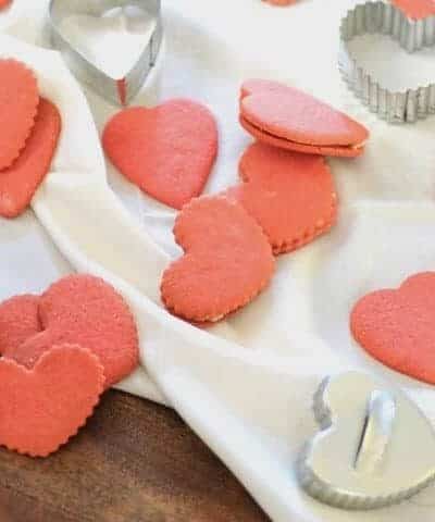Pink heart shaped Valentines Sugar Cookies on a white wrinkled cloth with heart shaped cookie cutters