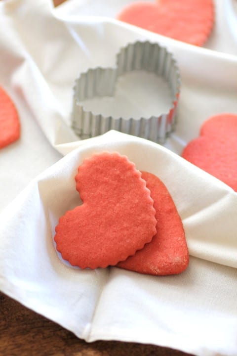 Pink Valentine Heart Cookies on a wrinkled white table cloth with a heart shaped cookie cutter