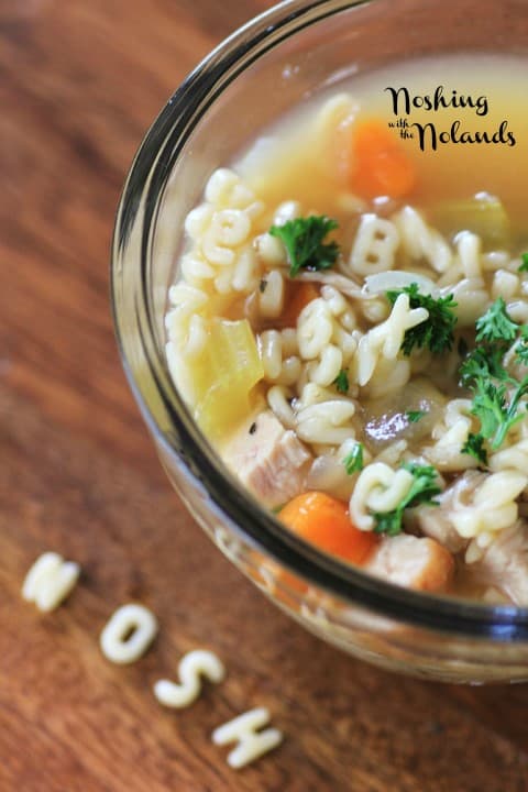 Alphabet Soup in a clear glass bowl with the noodles spelling NOSH on the board in front of the bowl