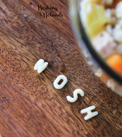 Alphabet Soup in a clear glass bowl with the noodles spelling NOSH on the board in front of the bowl