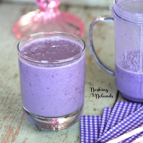 Banana and Blackberry Smoothie in a short glass with a red and white paper straw on a green board