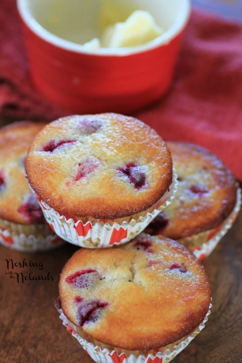 Cranberry Lemon Almond Muffins stacked on a wooden board with a red bowl with butter in it behind