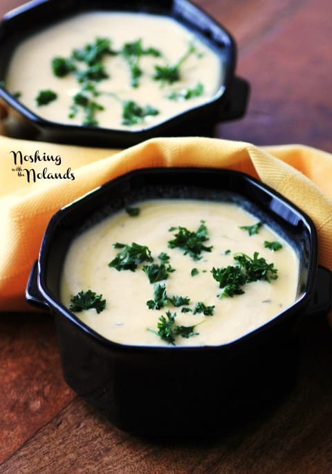 2 black bowls of Cream of Pumpkin Soup on a wooden board garnished with chopped parsley