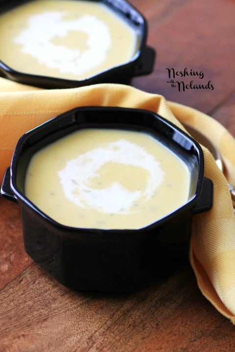 Cream of Pumpkin Soup in a black bowl on a wooden board with a gold cloth napkin
