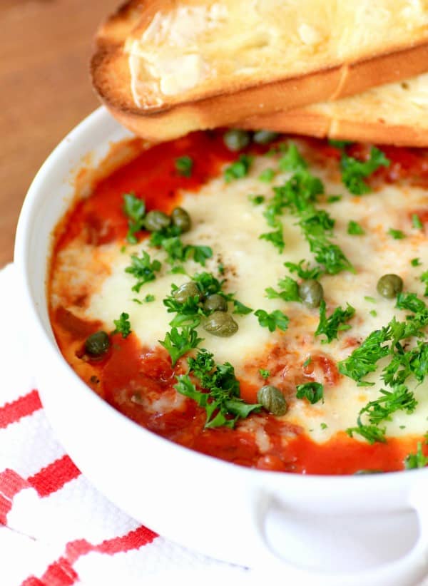 Eggs in Purgatory garnished with parsley and capers with toast in a white bowl