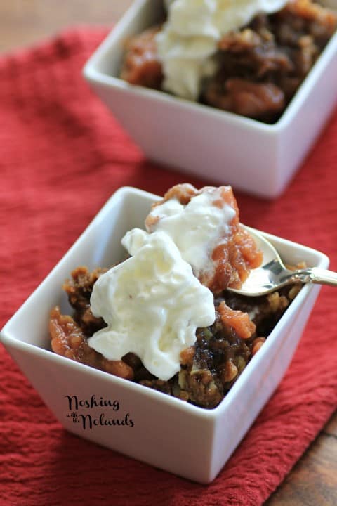 Slow Cooker Apple Crisp in a small white bowl with whipped cream and a spoon