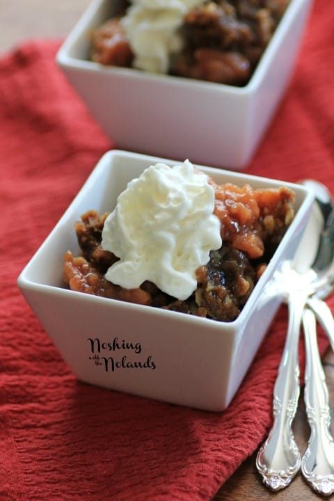 Slow Cooker Apple Crisp in a small white bowl with whipped cream and a spoon