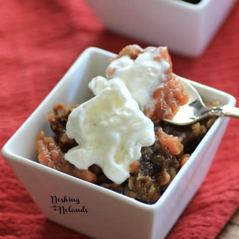 Slow Cooker Apple Crisp in a small white bowl with whipped cream and a spoon