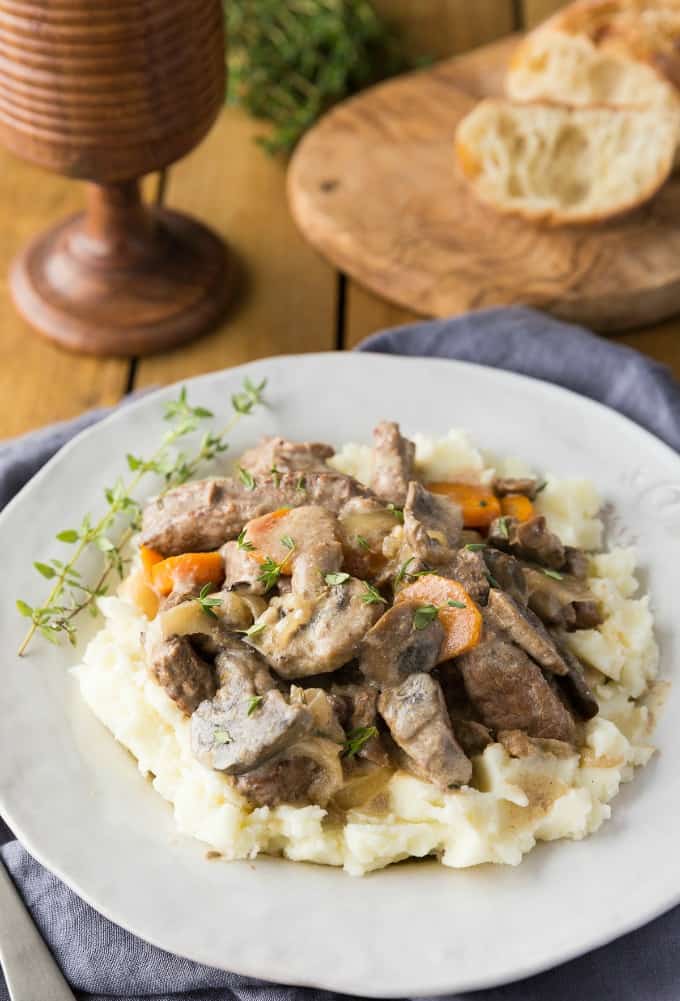 Slow Cooker Beef Stroganoff over mashed potatoes on a white plate with fresh thyme as garnish