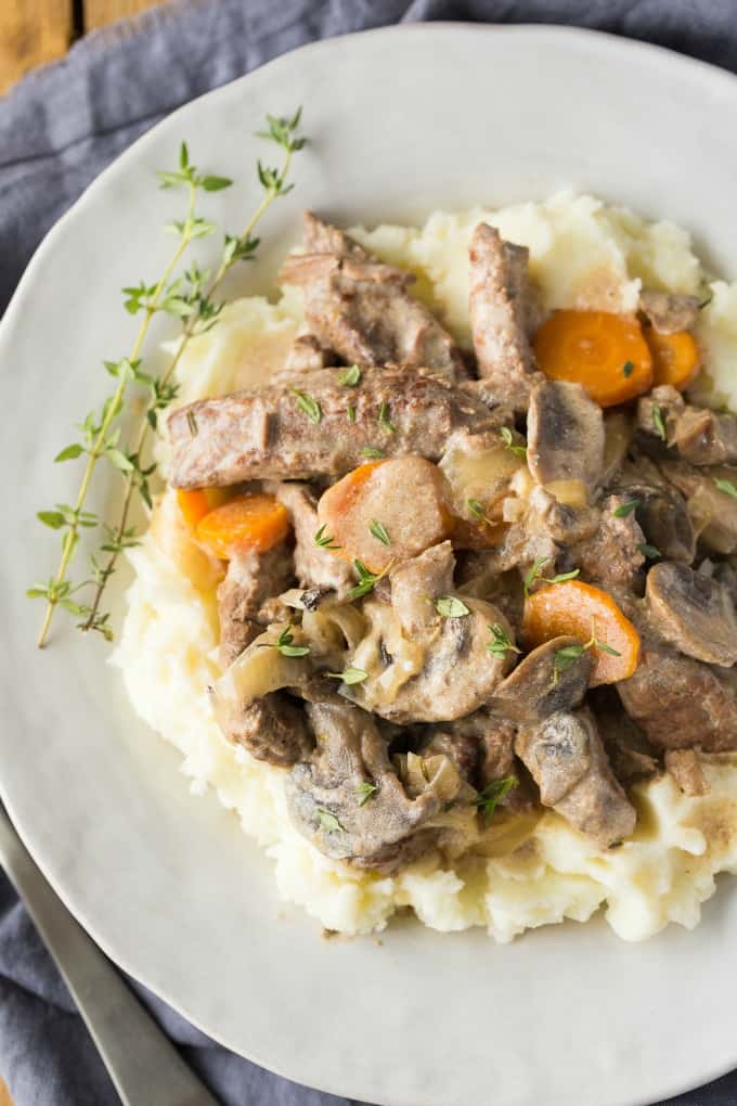 Slow Cooker Beef Stroganoff over mashed potatoes on a white plate