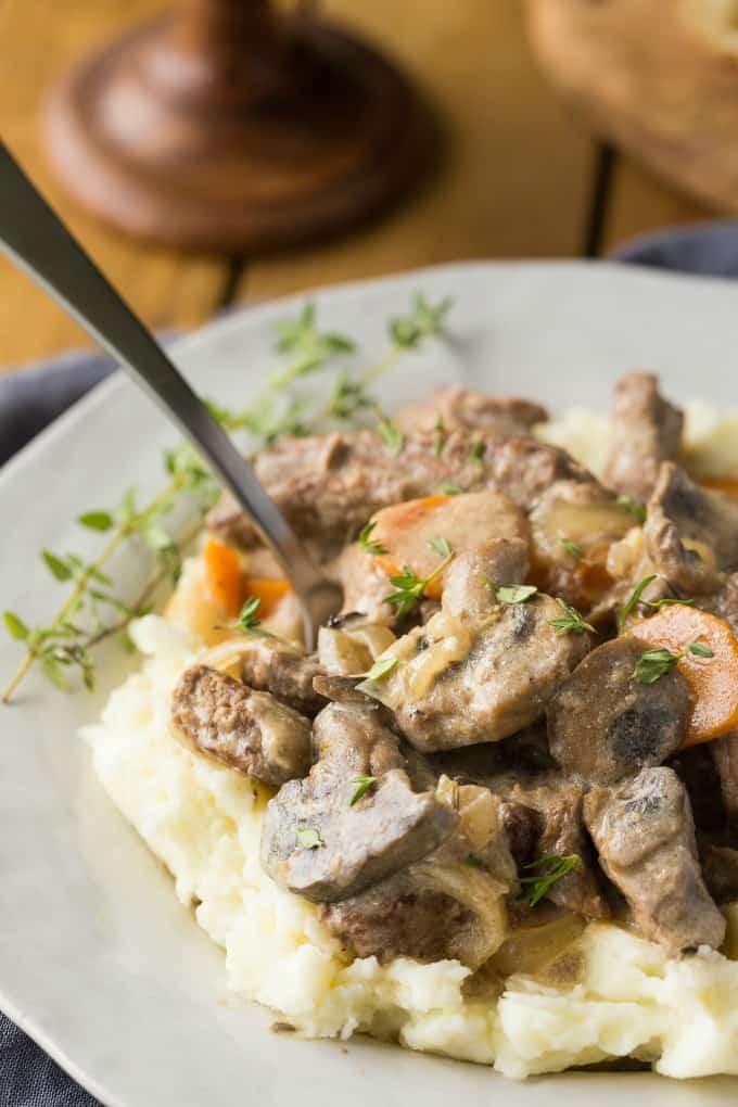 Slow Cooker Beef Stroganoff on top of mashed potatoes on a white plate with a fork