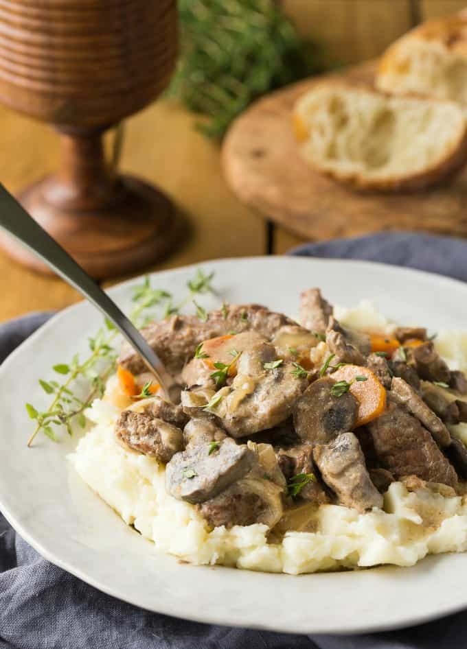 Slow Cooker Beef Stroganoff over mashed potatoes on a white plate with a fork