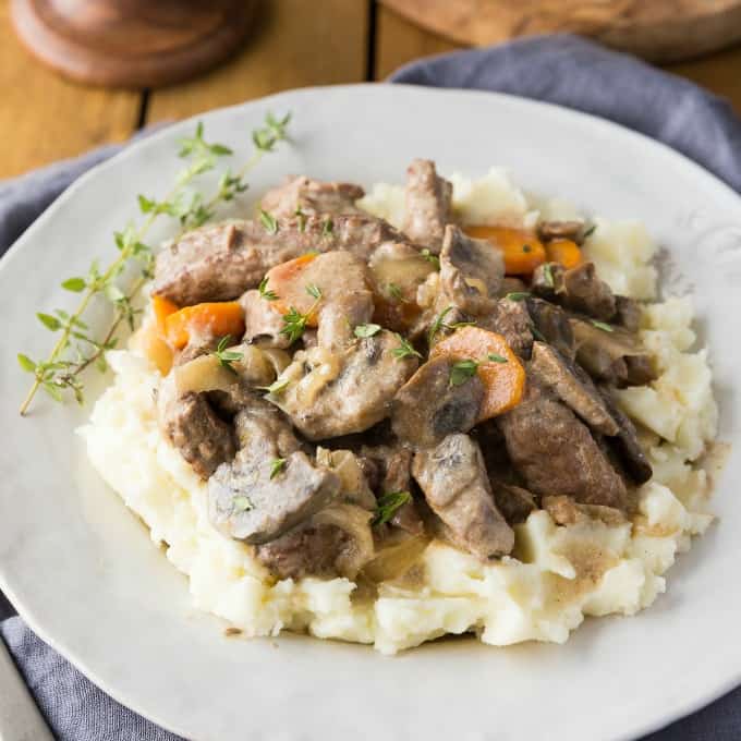 Slow Cooker Beef Stroganoff over mashed potatoes on a white plate