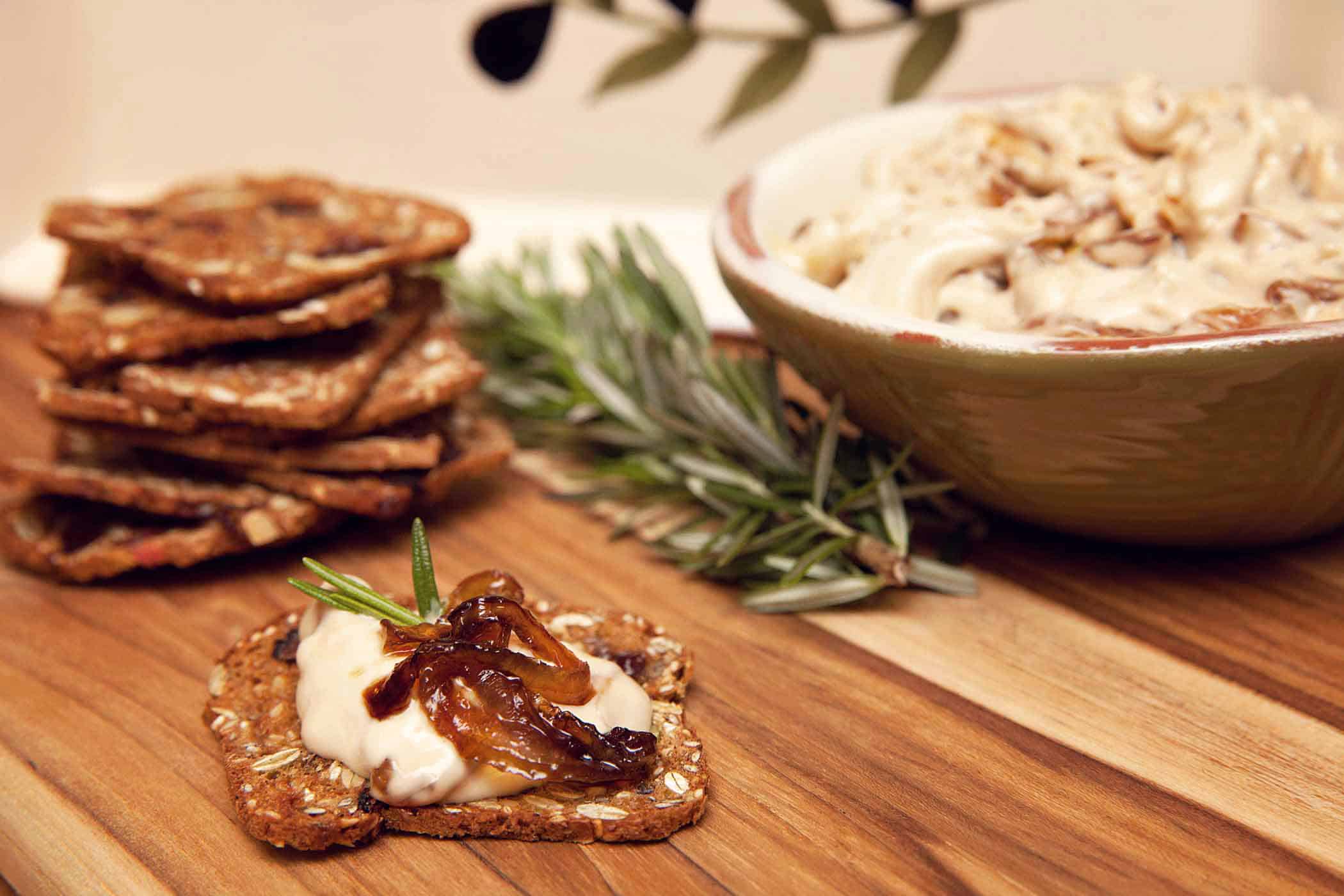 Caramelized onion & blue cheese dip on a whole grain cracker on a cutting board