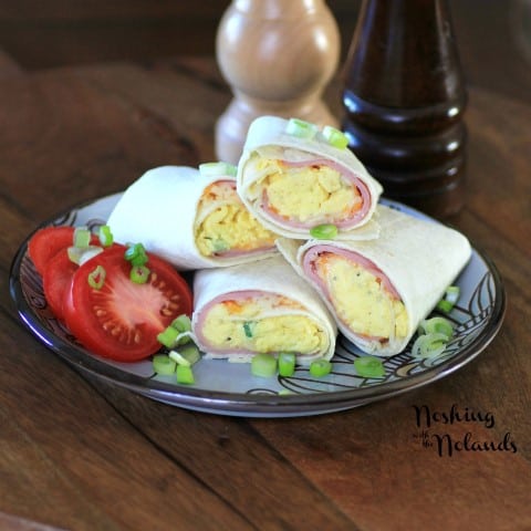 Egg Wraps cut in half and stacked on a grey and brown plate garnished with sliced tomato and chopped green onions 