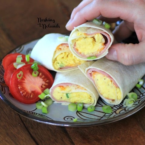 Egg Wraps cut in half and stacked on a grey and brown plate garnished with sliced tomato and chopped green onions 