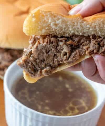 1/2 a bun of Slow Cooker Beef Dip held over a small bolw of Au Jus ready to be dipped