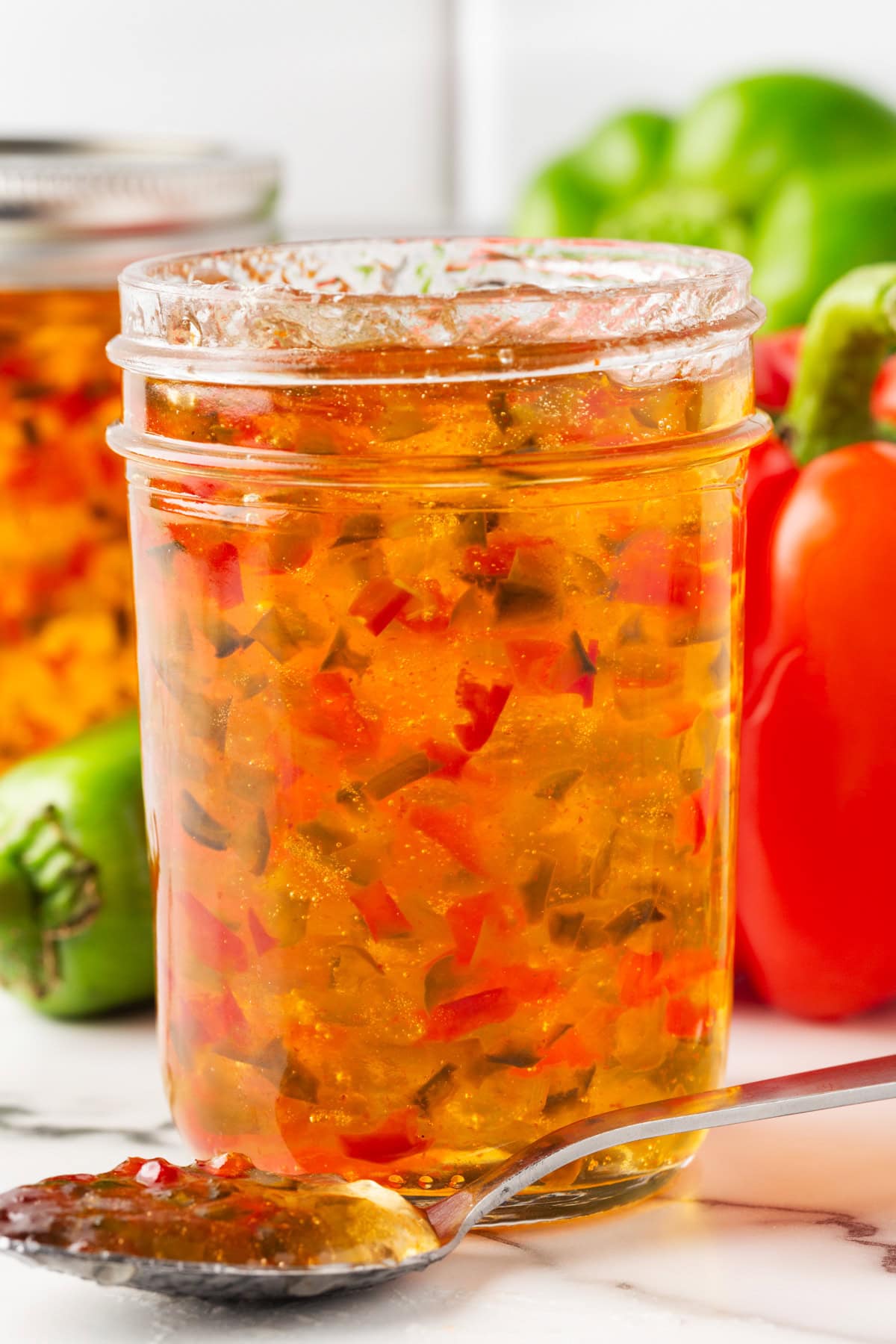 An open jar of red and green pepper jelly with a spoonful below. 