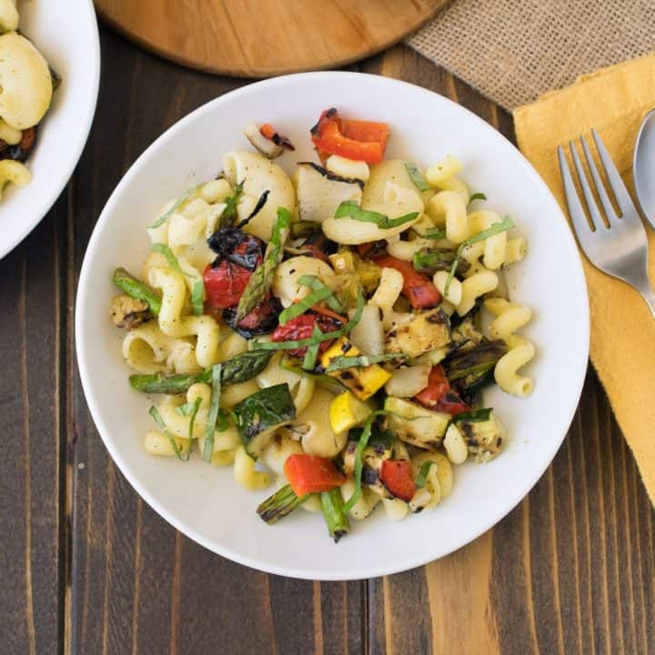 Grilled spring vegetable pasta salad in a white bowl with a fork and spoon beside the bowl