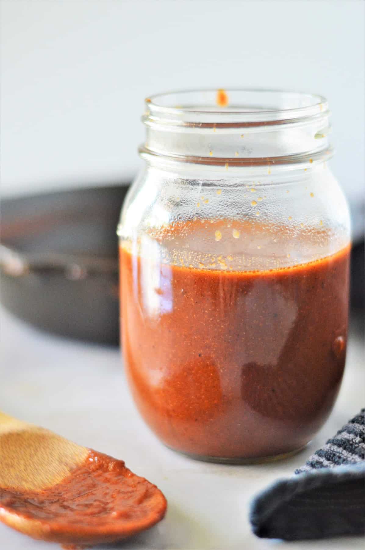 Homemade Enchilada Sauce in a jar with a wooden spoon with sauce on it. 