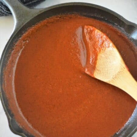 Homemade Enchilada Sauce in a cast iron pan with a wooden spoon.