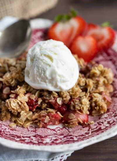 Strawberry Rhubarb Crisp on a plate topped with vanilla ice cream and sliced strawberries on the side.