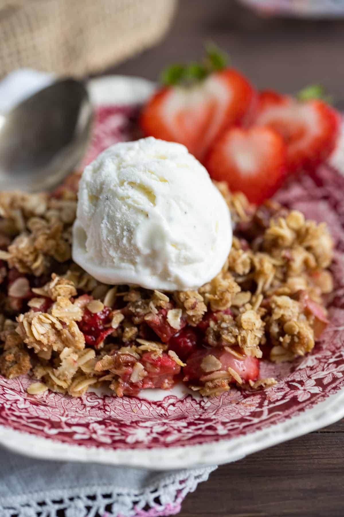 Strawberry Rhubarb Crisp on a plate topped with vanilla ice cream and sliced strawberries on the side.