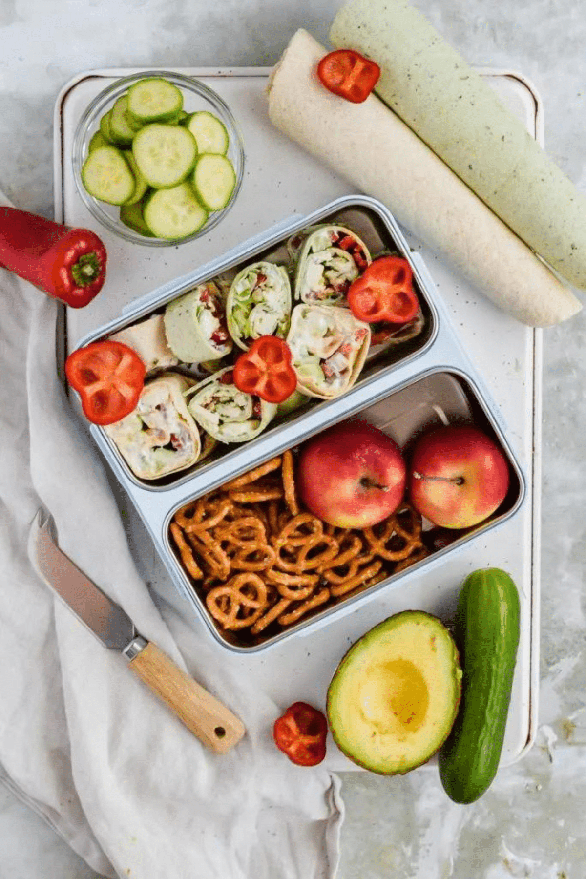 Mediterranean Pinwheels served in a lunchbox with pretzels and apples.