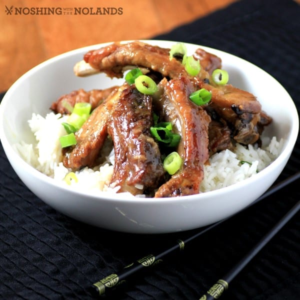 Sweet and Sour Ribs served in a white bowl over rice and garnished with chopped green onions