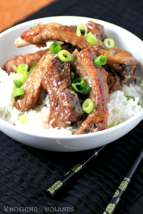 Sweet and Sour Ribs served in a white bowl over white rice garnished with chopped green onions